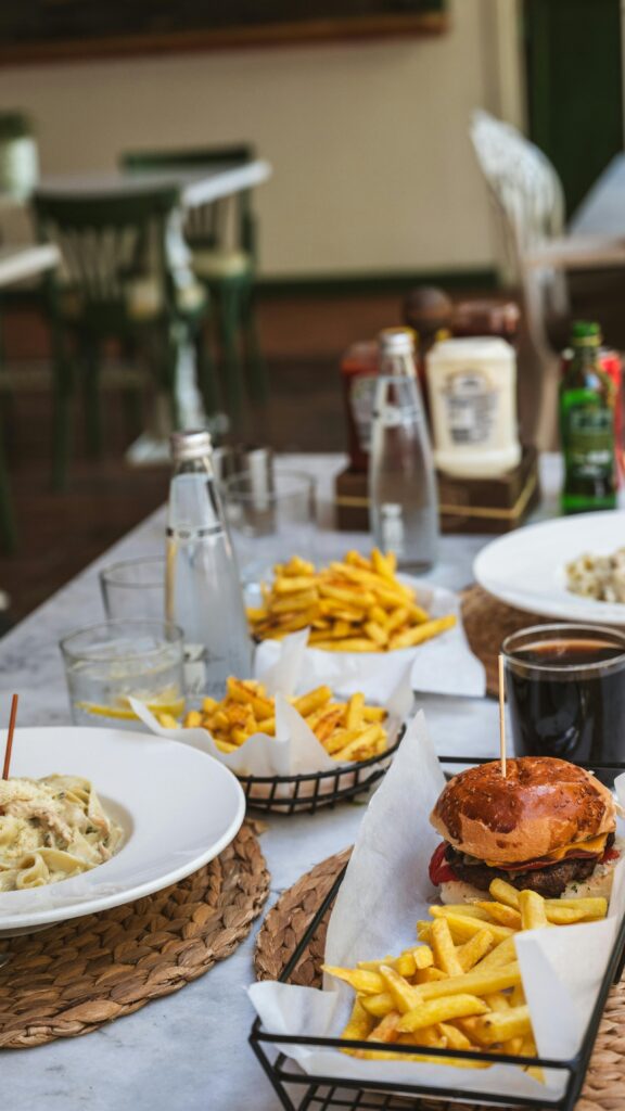 A table set for an outdoor meal featuring burgers, pasta, and fries, creating a casual dining ambiance.
