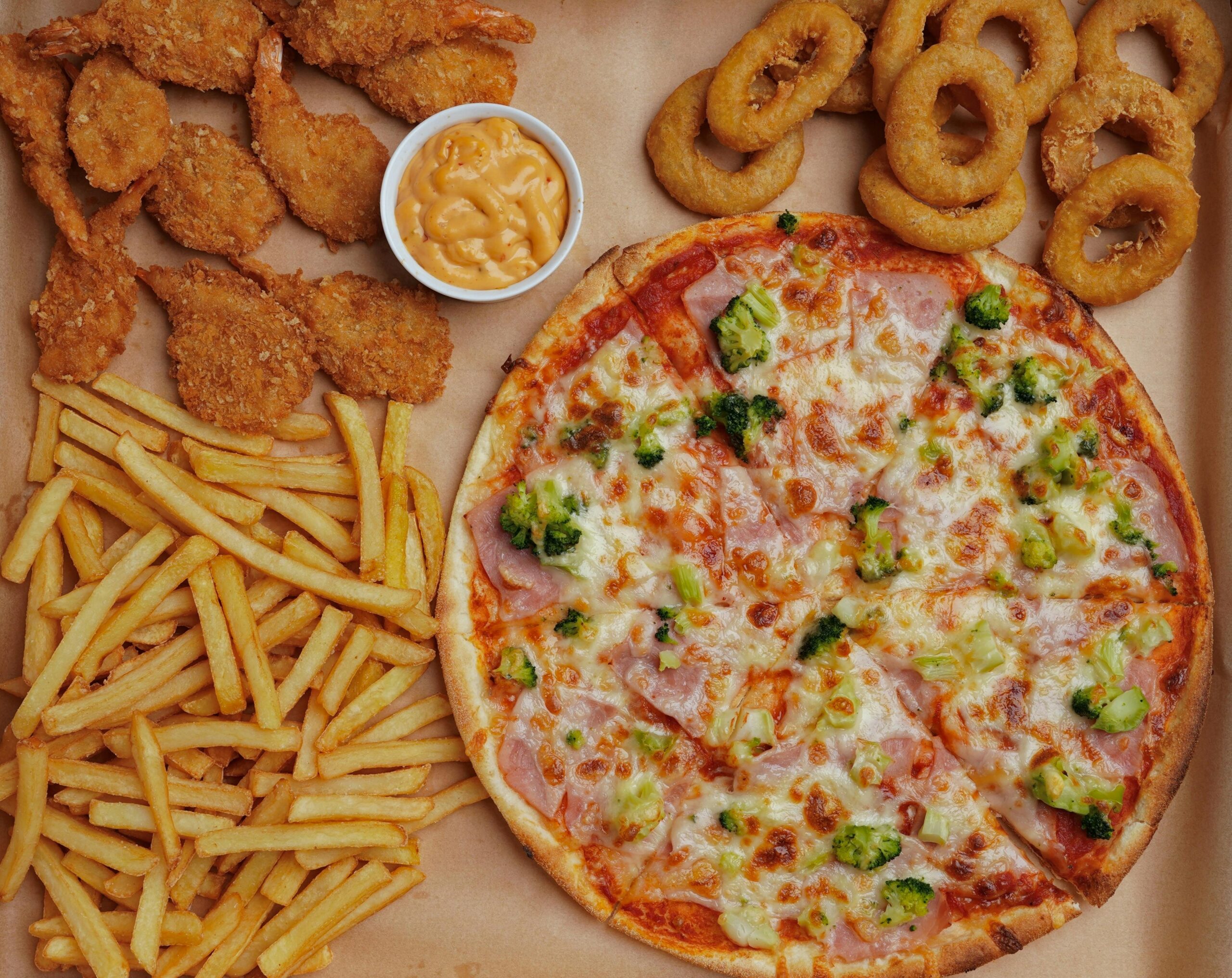 A visually appetizing array of pizza, fries, onion rings, shrimp and cheese dip.